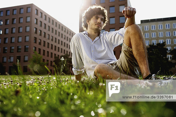 Young man relaxing on lawn  in background high rise buildings
