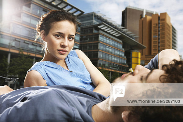 Germany  Berlin  Young couple lying in meadow  high rise buildings in background