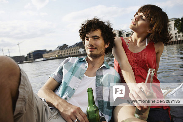 Germany  Berlin  Young couple on motor boat  holding bottles  portrait  close-up