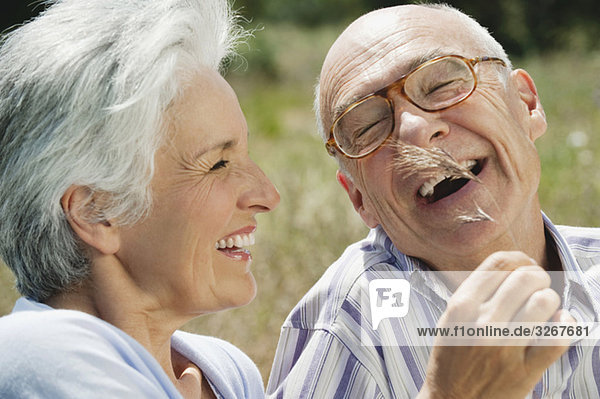 Spain  Mallorca  Senior couple  Woman tickling man with blade of grass  laughing  portrait  close-up