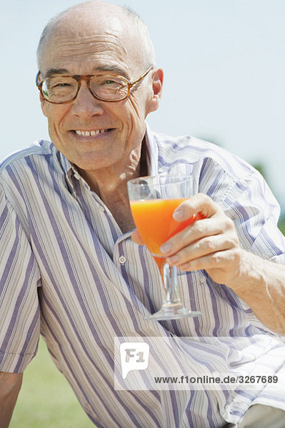 Spain  Mallorca  Senior man holding glass with orange juice  portrait