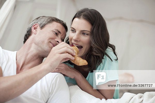 Couple in bedroom  woman biting into croissant