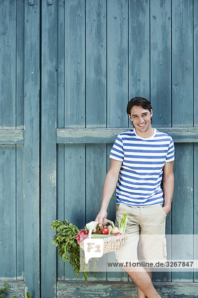 Mann vor der Scheunentür hält Korb mit frischem Gemüse  lächelnd  Portrait