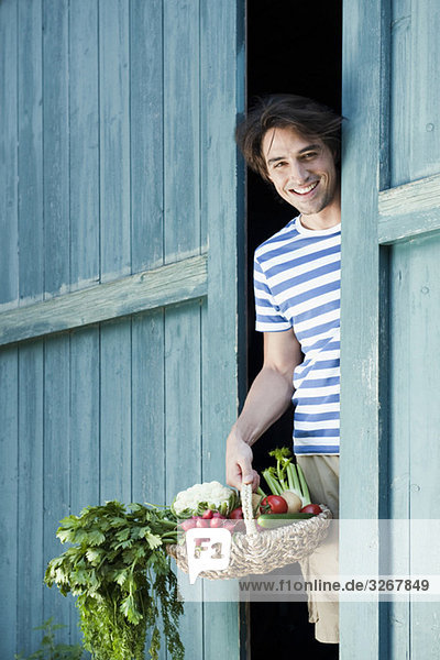Mann vor der Scheunentür hält Korb mit frischem Gemüse  lächelnd  Portrait