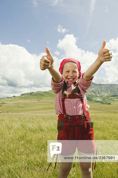 Italy  Seiseralm  Girl (8-9) in meadow giving thumbs up  smiling  portrait