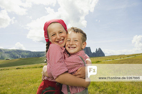 Italy  Seiseralm  Boy (6-7) and girl (8-9) in field  embracing  smiling  portrait