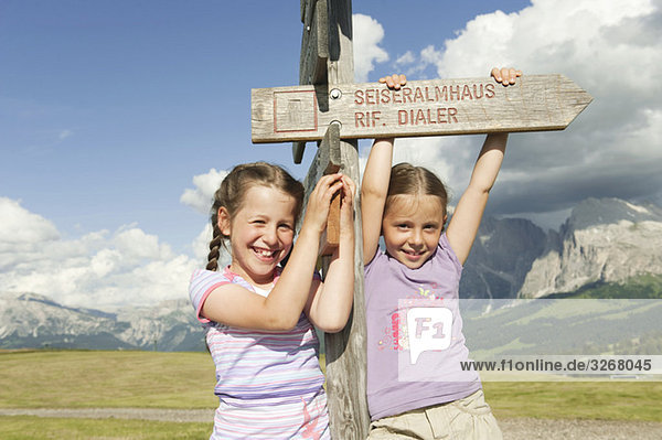 Italy  Seiseralm  Girls (6-9) holding sign post  smiling  portrait