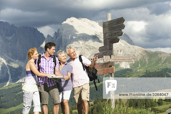 Italy  Seiseralm  Men and women holding map looking at sign post  smiling