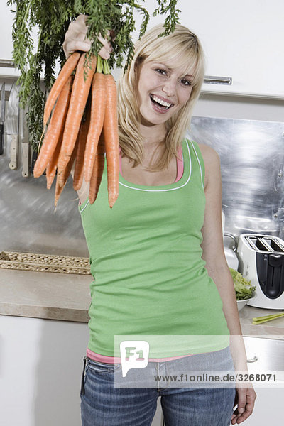 Junge Frau in der Küche mit Karottenstrauß  lächelnd  Portrait