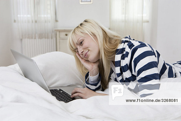 Junge Frau auf dem Bett liegend mit Laptop  lächelnd