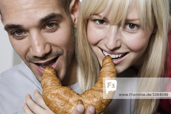Deutschland  Berlin  Junges Paar beim Croissantessen  lächelnd  Nahaufnahme