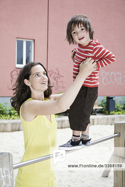 Deutschland  Berlin  Mutter hält Sohn (2-3) auf dem Spielplatz  lächelnd