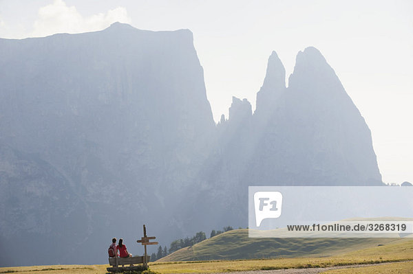 Italien  Südtirol  Seiseralm  Paar auf Bank sitzend  Rückansicht