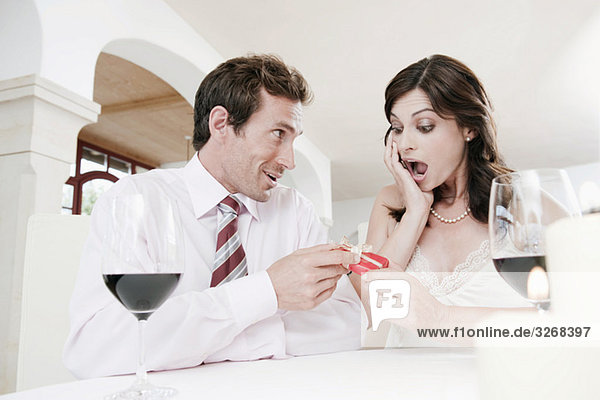 Couple sitting at table in restaurant  woman holding gift parcel