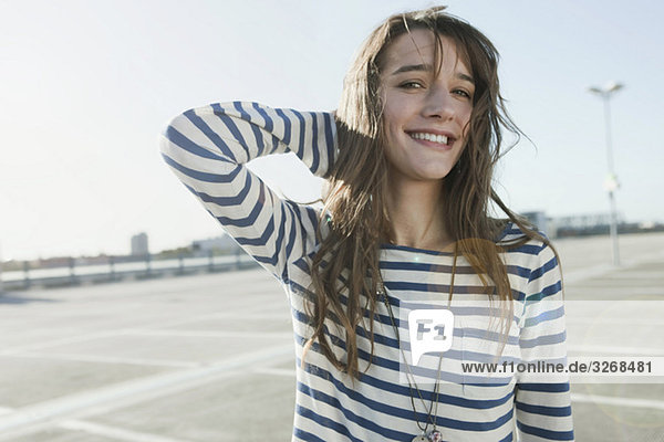 Young woman on deserted parking level  hand on head  smiling  portrait