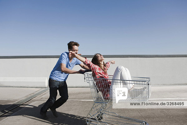 Young man pushing young woman in shopping cart