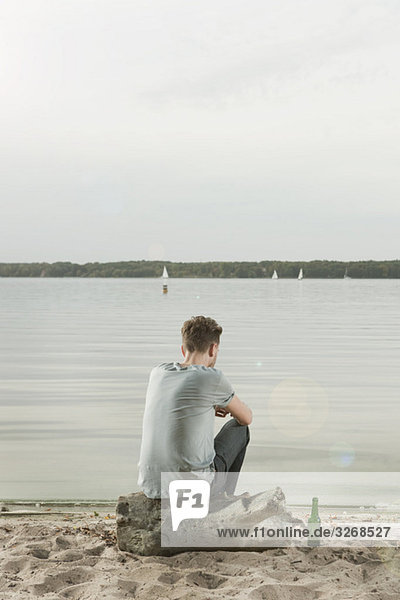 Young man sitting on rock near lake  rear view