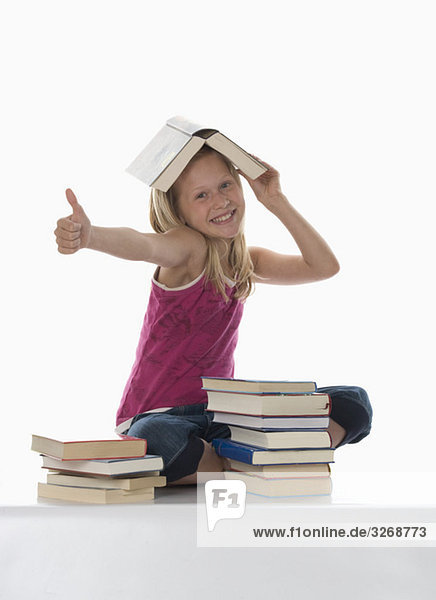 Porträt eines Mädchens (10-11) mit gestapelten Büchern  Daumen nach oben
