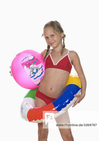 Girl (10-11) wearing bikini  holding floating tire and beachball
