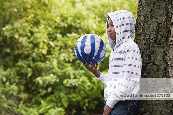 Boy leaning on tree with ball