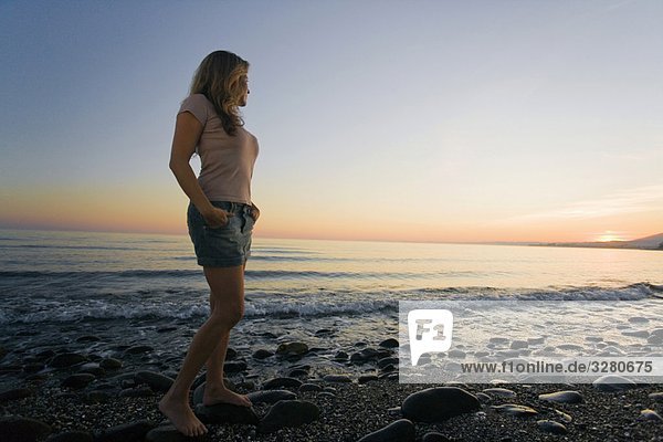 Frau am Strand beobachtet Sonnenuntergang im niedrigen Winkel