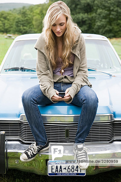 Young woman sitting on car with cellphone