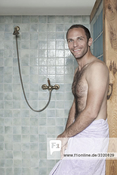 Ein Mann in ein Handtuch gewickelt  der bei einer Dusche in einem Spa steht.