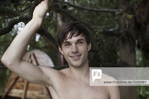 A wet man holding onto a branch  hot tub in background