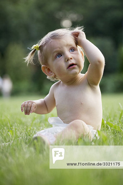 Ein kleines Mädchen sitzt auf Gras in einer Windel.