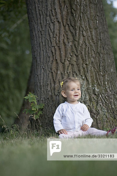 Ein kleines Mädchen sitzt unter einem Baum und schaut weg.