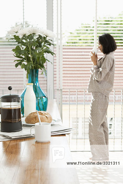 Breakfast on a kitchen counter and a women in pajamas drinking coffee