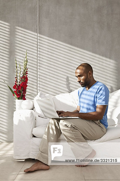 A casually dressed man sitting on a sofa using a laptop
