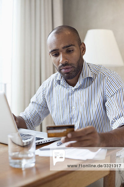 A man with a laptop looking at a credit card in his hand