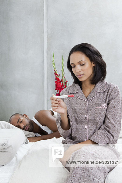 A woman looking at a pregnancy test while her boyfriend sleeps