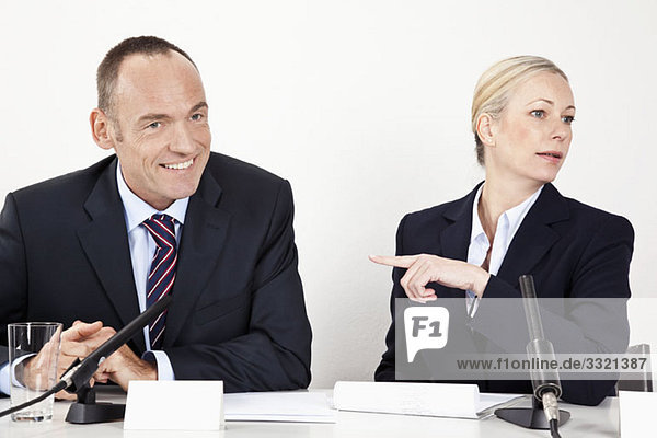 Ein Mann und eine Frau sitzen an einem Schreibtisch mit Mikrofonen.