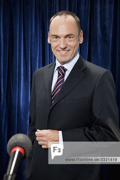 Porträt eines Mannes im Anzug hinter einem Mikrofon