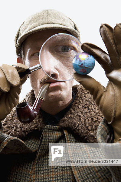 A man dressed up as Sherlock Holmes looking at a tiny globe through a magnifying glass