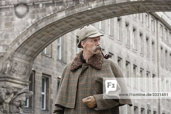 Ein als Sherlock Holmes verkleideter Mann steht unter einem Gebäudebogen und schaut weg.