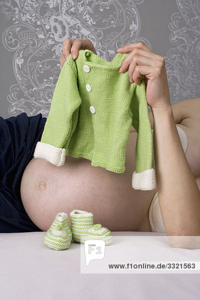 Eine schwangere Frau hält einen Babypullover hoch  Mittelteil