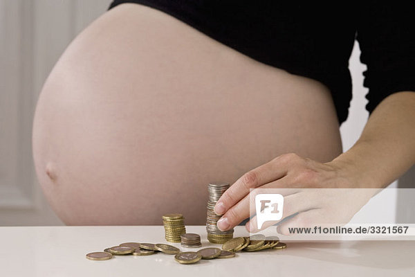 Eine schwangere Frau beim Stapeln von EU-Münzen  Mittelteil  Fokus auf der Hand