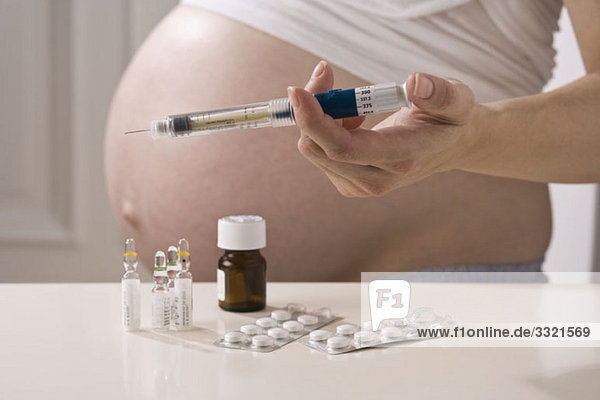 Eine schwangere Frau  die eine Spritze über andere pränatale Medikamente hält.