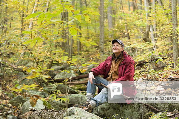Ein Mann sitzt auf einem Felsen im Wald.