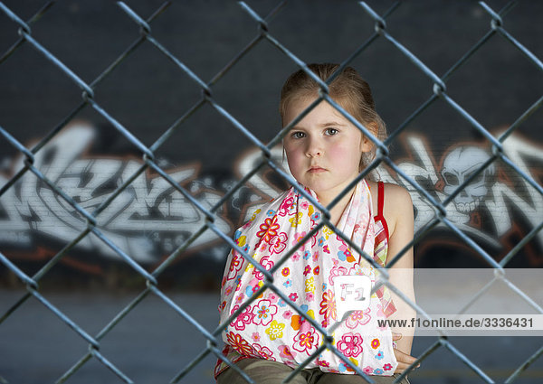 Little girl with broken arm behind fence with graffiti in background