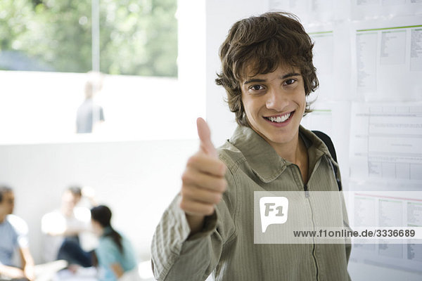 Male college student giving thumbs up  bulletin board in background