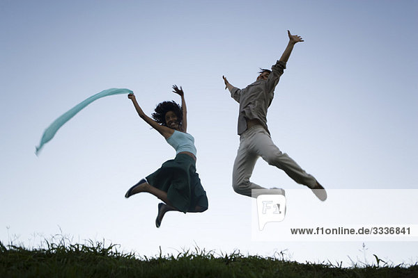 Junges Paar springt übermütig mit erhobenen Armen und trägt Freudenausdrücke.