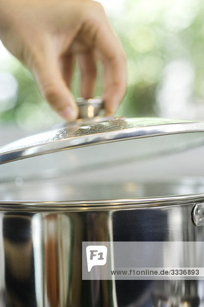 Person removing lid from cooking pot