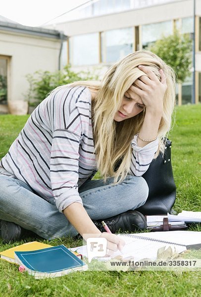 Konzentrierte Frau sitzt auf dem Rasen und schreibt in einem Notizblock.