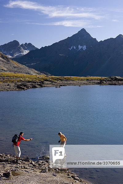 10874061 Switzerland swiss walk hike two pair couple stones throw Graubunden Grisons Bundnerland autumn Fluelapass persons scenery lake black horn mountains nature Davos footpath mountain lake canton