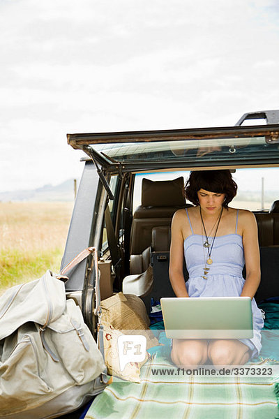 Junge Frau mit Laptop im hinteren Teil des Geländewagens