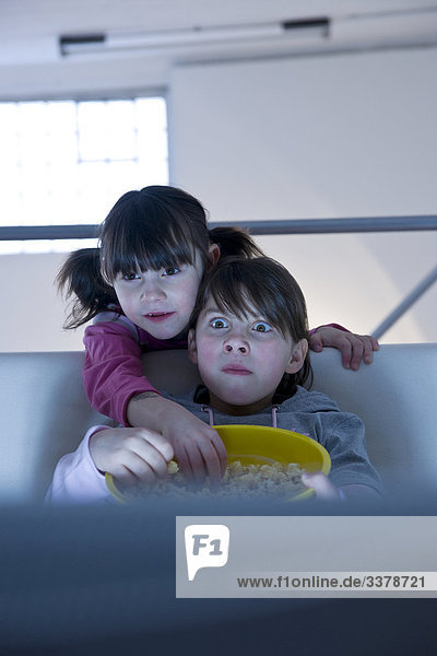 Zwei Mädchen mit einer Schüssel Popcorn vor dem Fernseher  Frontalansicht